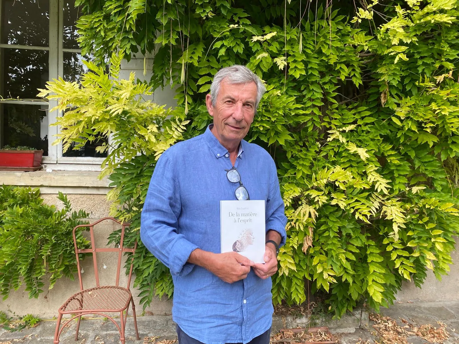 Marc Leguillon tenant son livre « De la matière à l’esprit » devant une glycine